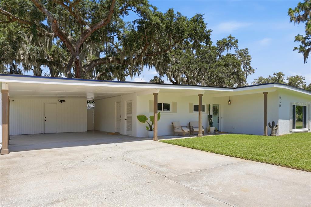 A white single-story house features a large carport, a front lawn, and mature oak trees — 5120 MORTIER AVENUE, BELLE ISLE, FL