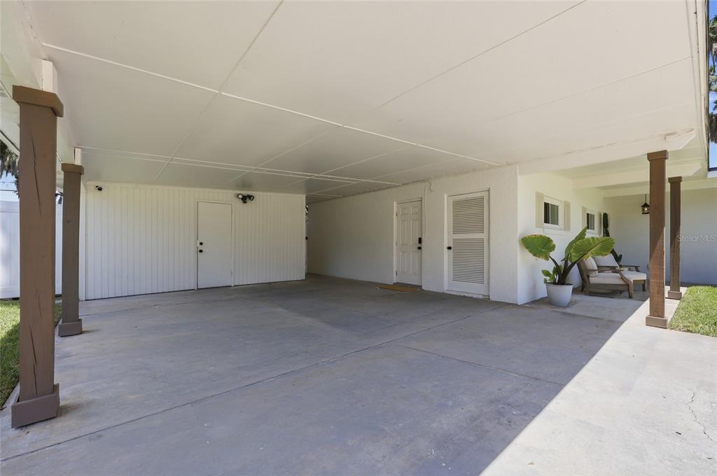 A covered concrete carport features white walls, several doors, and wooden support columns — 5120 MORTIER AVENUE, BELLE ISLE, FL
