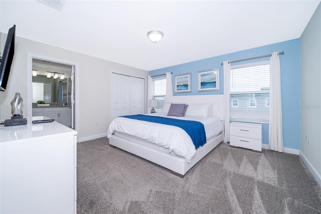 A bedroom features a king bed, blue accent wall, gray carpeting, and an attached bathroom — 212 OCEAN COURSE AVENUE, DAVENPORT, FL