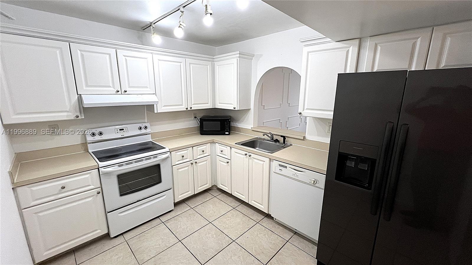 A kitchen features white cabinets, beige countertops, tile flooring, and a black refrigerator — 711 N Pine Island Rd # 211, Plantation FL 33324, PLANTATION, FL