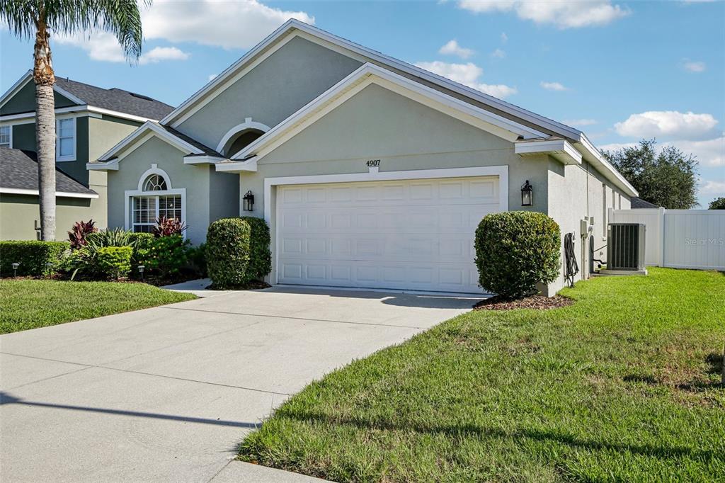 A single-story house with a two-car garage, light-colored stucco siding, and a manicured lawn — 4907 58TH TERRACE E, BRADENTON, FL