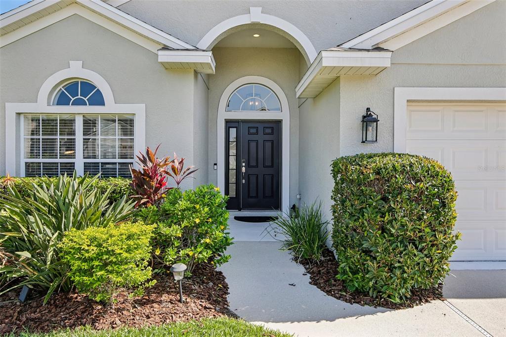 The exterior of a house features a black front door, arched windows, and landscaping — 4907 58TH TERRACE E, BRADENTON, FL