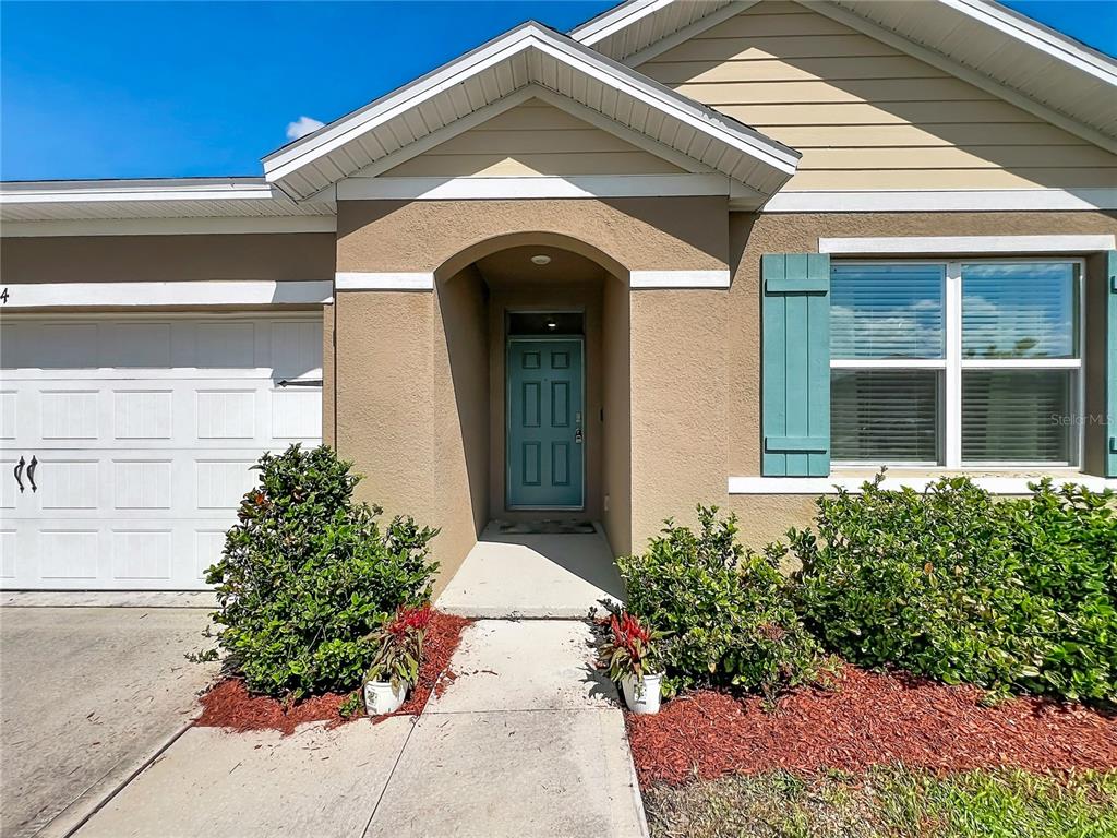 The exterior of a house features a teal front door, a garage, and landscaped bushes — 3974 MEKONG COURT, ST CLOUD, FL
