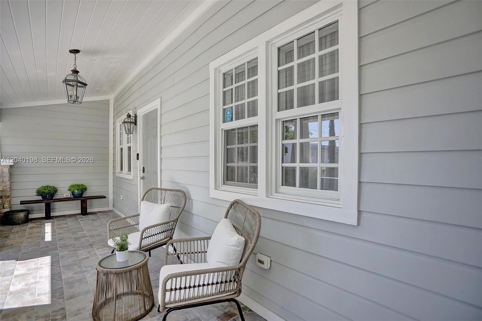 A covered porch features light gray siding, two wicker chairs, a small table, and windows — 421 NE 70th ST, Miami FL 33138, MIAMI, FL