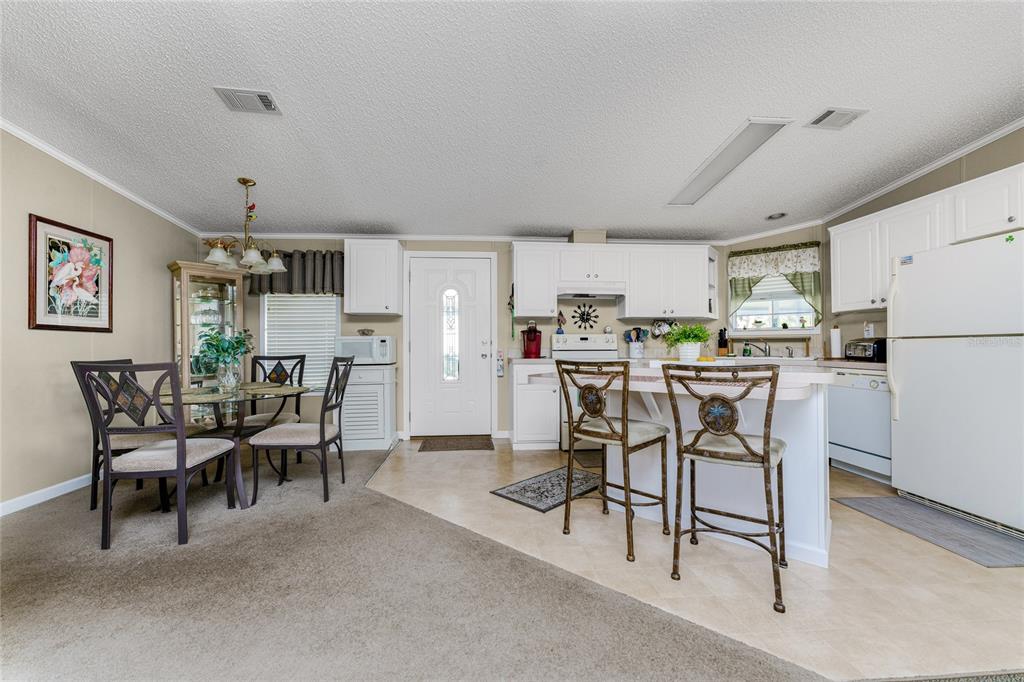 An open-concept kitchen and dining area features white cabinetry, a breakfast bar, and carpeted flooring — 24437 HARBORVIEW ROAD UNIT 62, PUNTA GORDA, FL