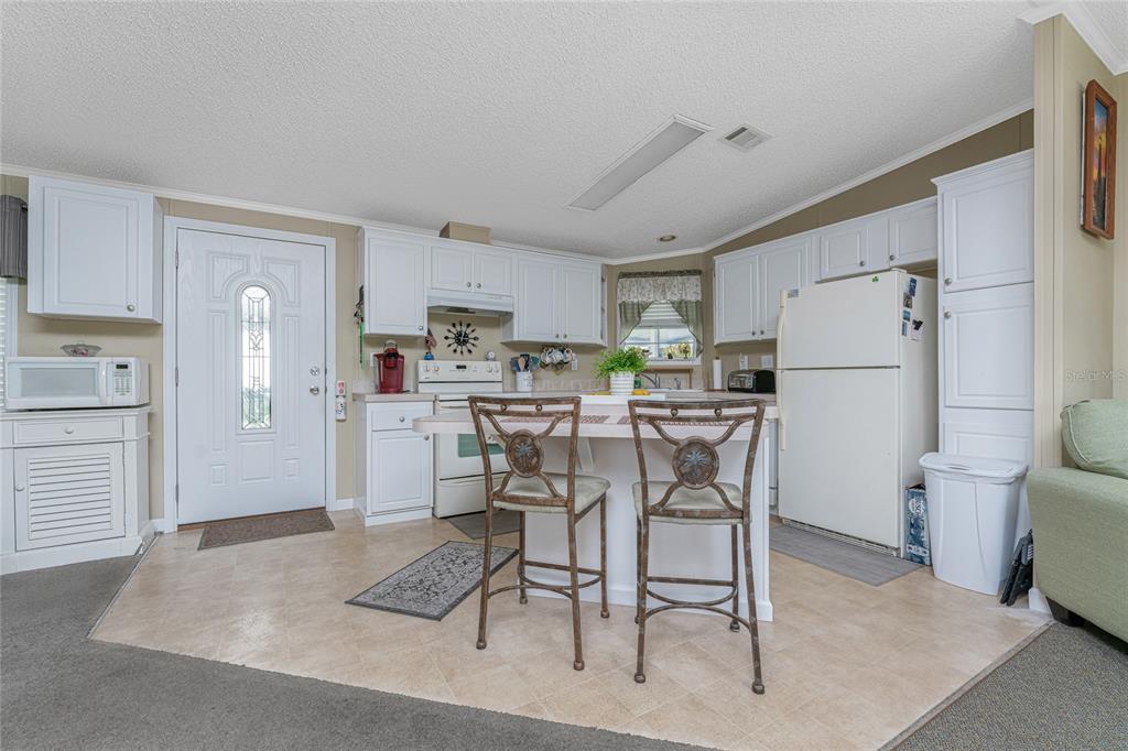 A kitchen features white cabinets, a central island with two chairs, and a white refrigerator — 24437 HARBORVIEW ROAD UNIT 62, PUNTA GORDA, FL