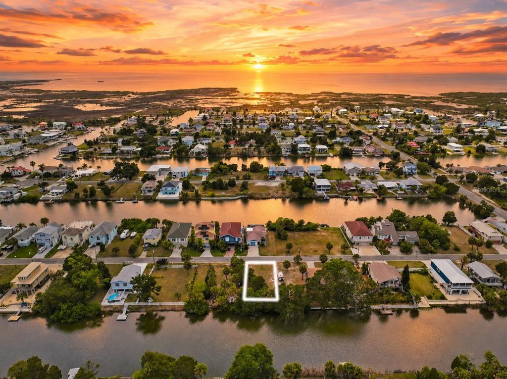 An aerial view shows a vacant waterfront lot highlighted by a white rectangle at sunset — 3240 SEA GRAPE DRIVE, HERNANDO BEACH, FL