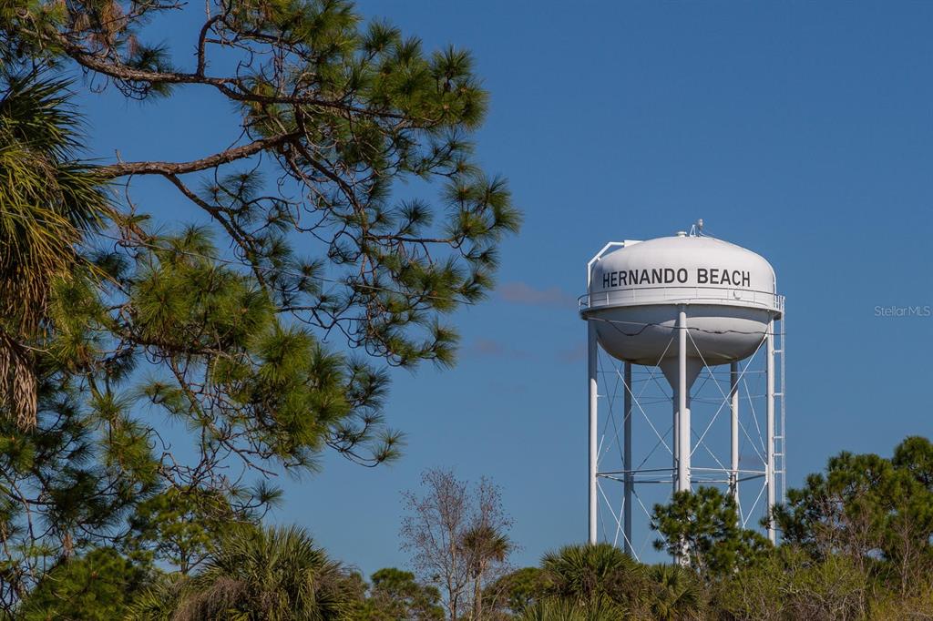 A white water tower labeled Hernando Beach stands against a clear blue sky — 3240 SEA GRAPE DRIVE, HERNANDO BEACH, FL