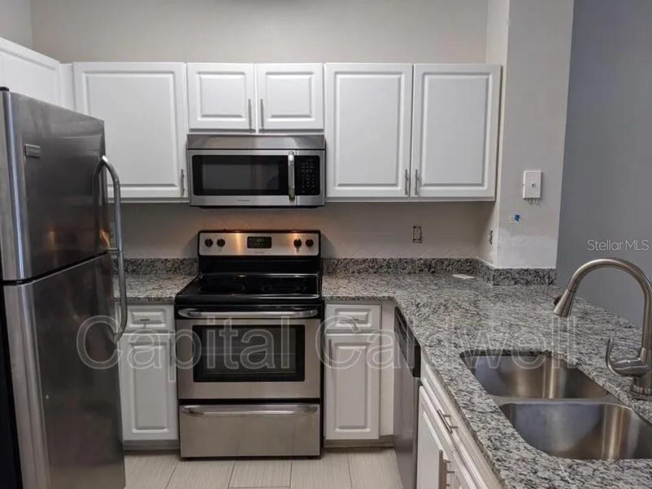A kitchen features white cabinets, stainless steel appliances, and speckled granite countertops — 1910 E PALM AVENUE UNIT 11213, TAMPA, FL