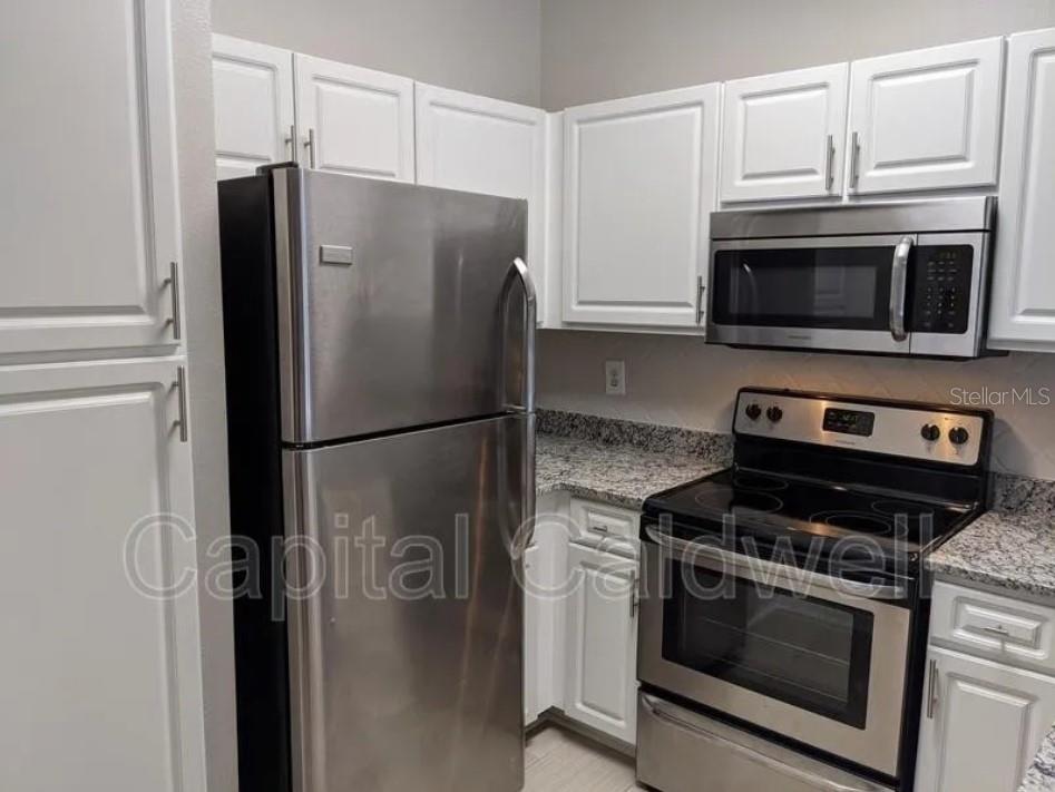 A kitchen features white cabinets, granite countertops, and stainless steel appliances — 1910 E PALM AVENUE UNIT 11213, TAMPA, FL