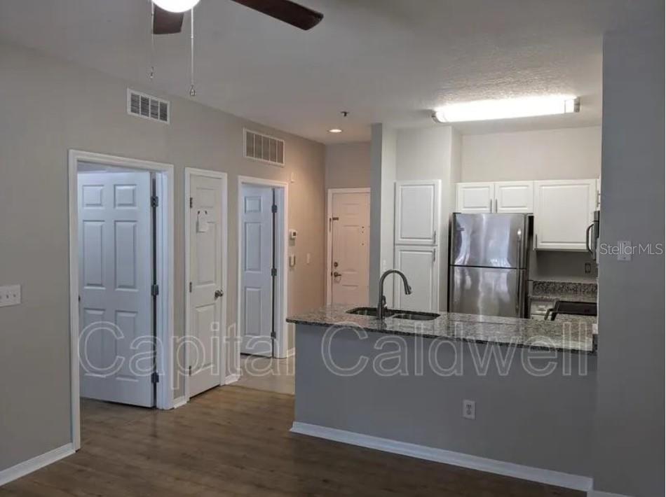 A kitchen with white cabinets, granite countertops, and stainless steel appliances opens to a hallway — 1910 E PALM AVENUE UNIT 11213, TAMPA, FL