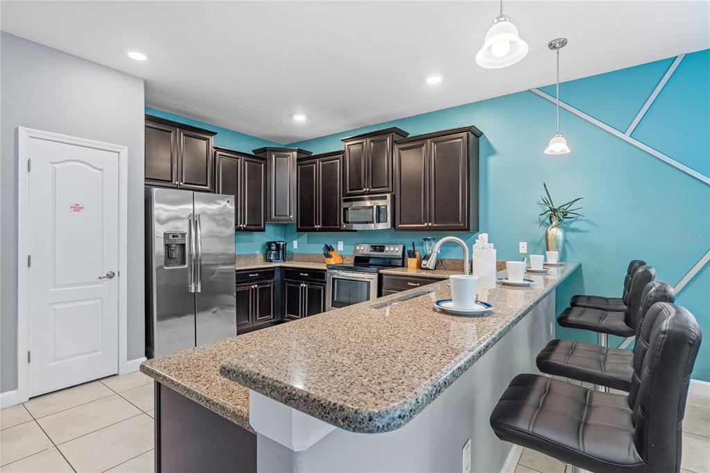 A kitchen features dark wood cabinets, granite countertops, stainless steel appliances, and a breakfast bar — 9158 WEDGE DRIVE, DAVENPORT, FL