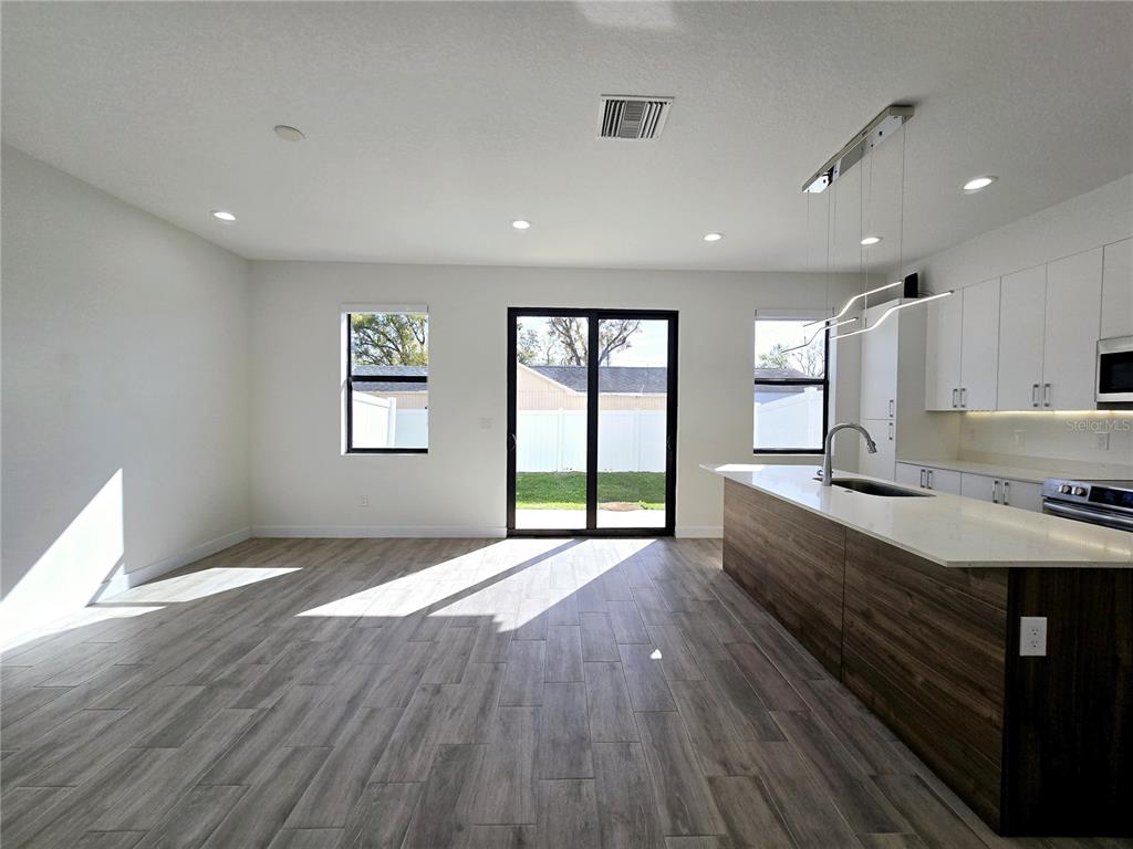 A kitchen and living area featuring wood-look tile floors, white cabinets, and a center island — 7573 GESUALDO COURT, TAMPA, FL