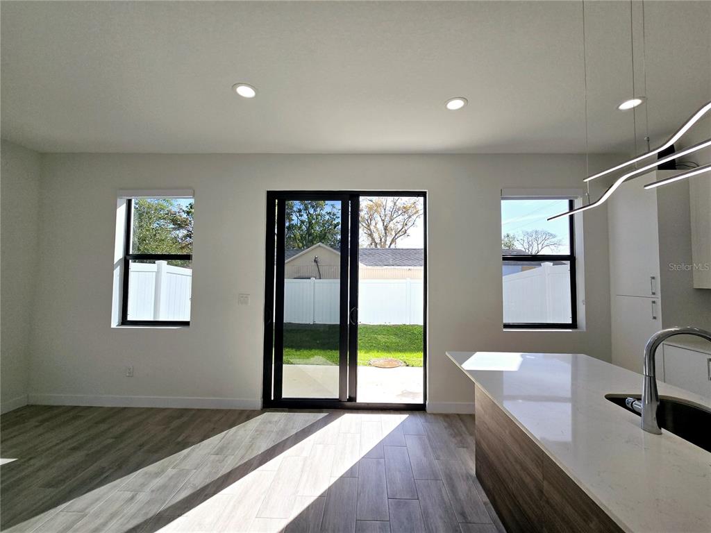 A modern kitchen and living area features wood-look tile flooring, white walls, and sliding doors — 7573 GESUALDO COURT, TAMPA, FL
