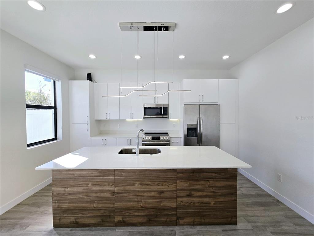 A modern kitchen features white cabinetry, stainless steel appliances, and a wood-paneled island with seating — 7573 GESUALDO COURT, TAMPA, FL
