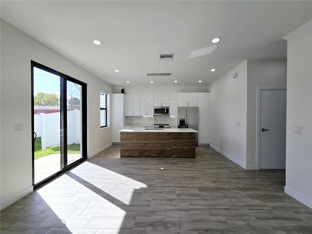 A modern kitchen features white cabinetry, a wood-paneled island, and sliding glass doors to outdoors — 7573 GESUALDO COURT, TAMPA, FL