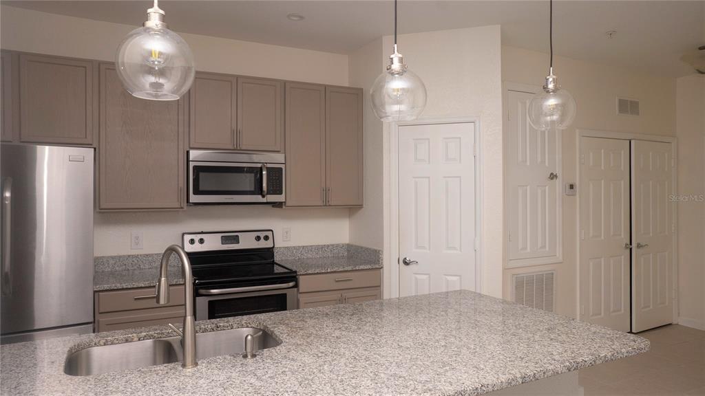 A kitchen features gray cabinets, granite countertops, stainless steel appliances, and three glass pendant lights — 6466 CAVA ALTA DRIVE UNIT 101, ORLANDO, FL