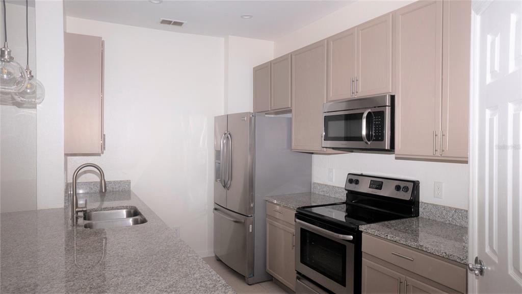 A kitchen features stainless steel appliances, granite countertops, and light-colored cabinets — 6466 CAVA ALTA DRIVE UNIT 101, ORLANDO, FL