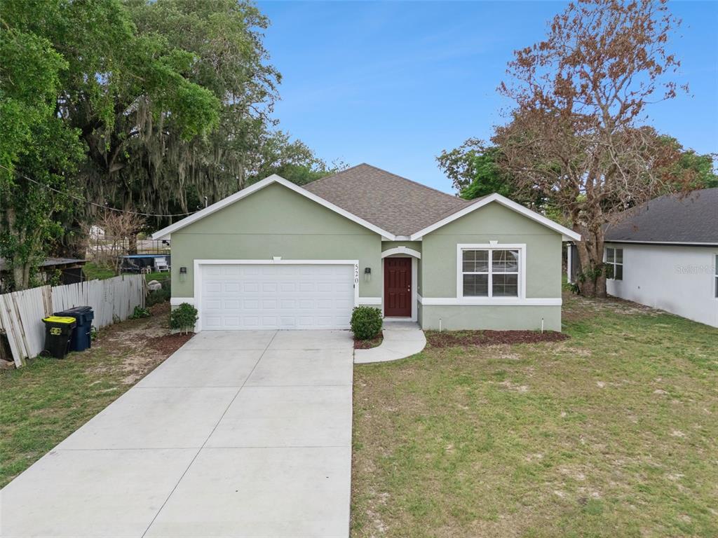 A single-story house with a green stucco exterior, a two-car garage, and a red door — 520 LEMON STREET, AUBURNDALE, FL