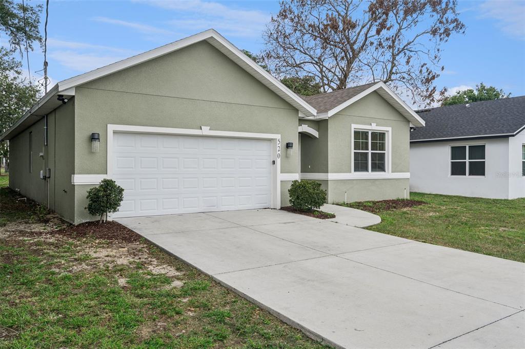 A single-story house with light green stucco siding, a white garage door, and a driveway — 520 LEMON STREET, AUBURNDALE, FL