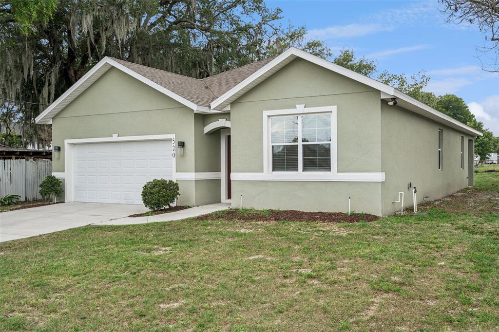 A single-story house with light green stucco siding, a two-car garage, and a front lawn — 520 LEMON STREET, AUBURNDALE, FL