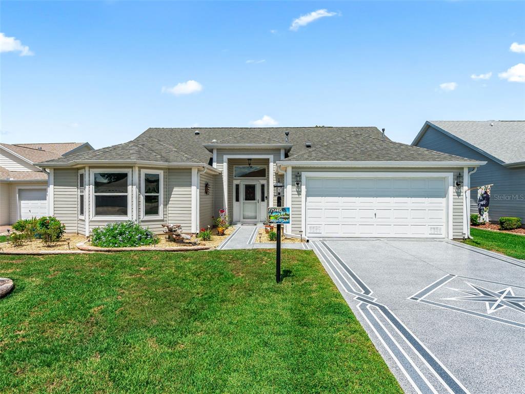 A single-story house with light siding, a two-car garage, and a decorative concrete driveway — 17946 SE 87TH MELROSE COURT, THE VILLAGES, FL