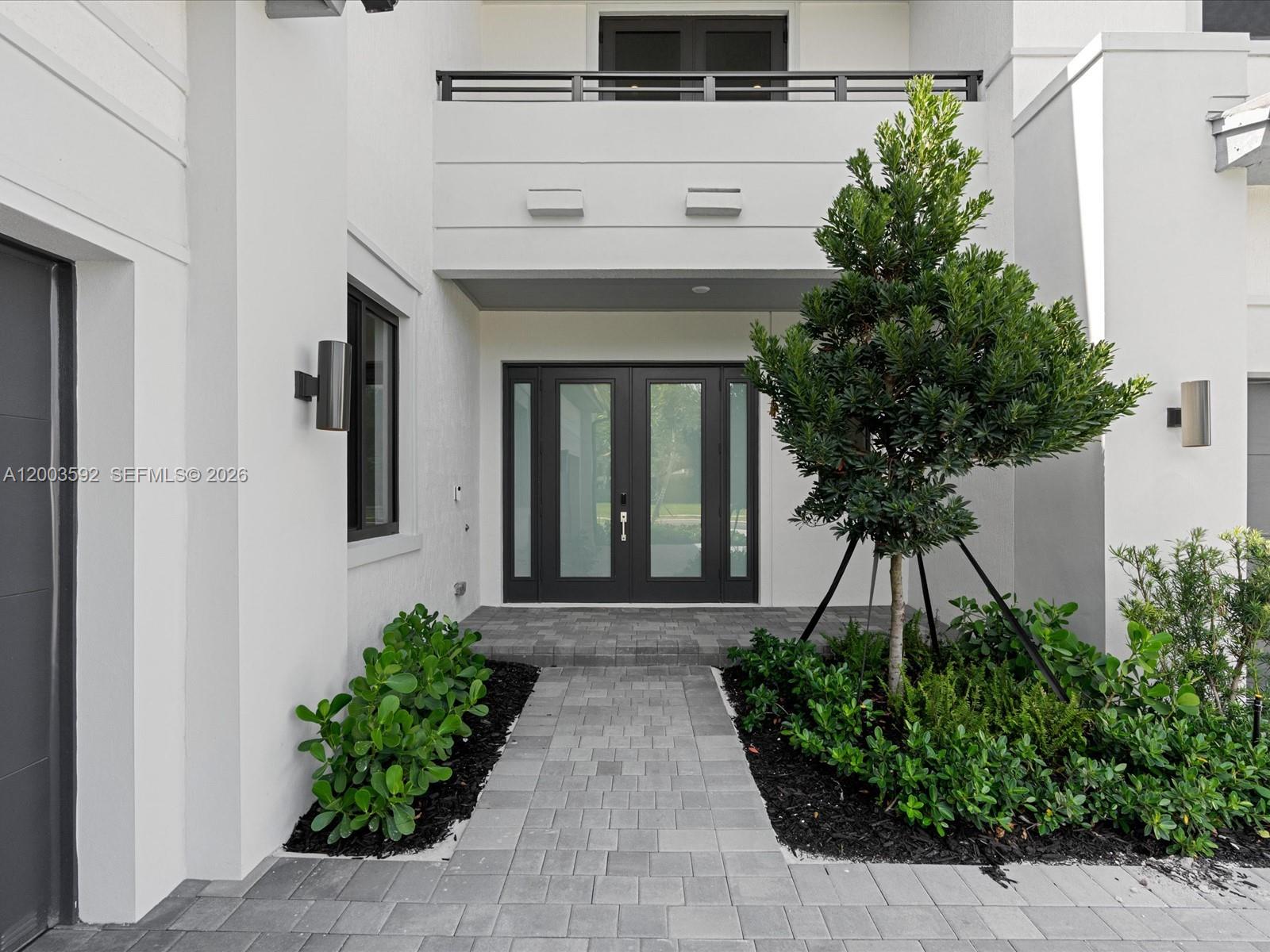 A modern white house entrance features a paved walkway, dark-framed double doors, and landscaping — 19602 NE 14 CT # 0, Miami FL 33179, MIAMI, FL