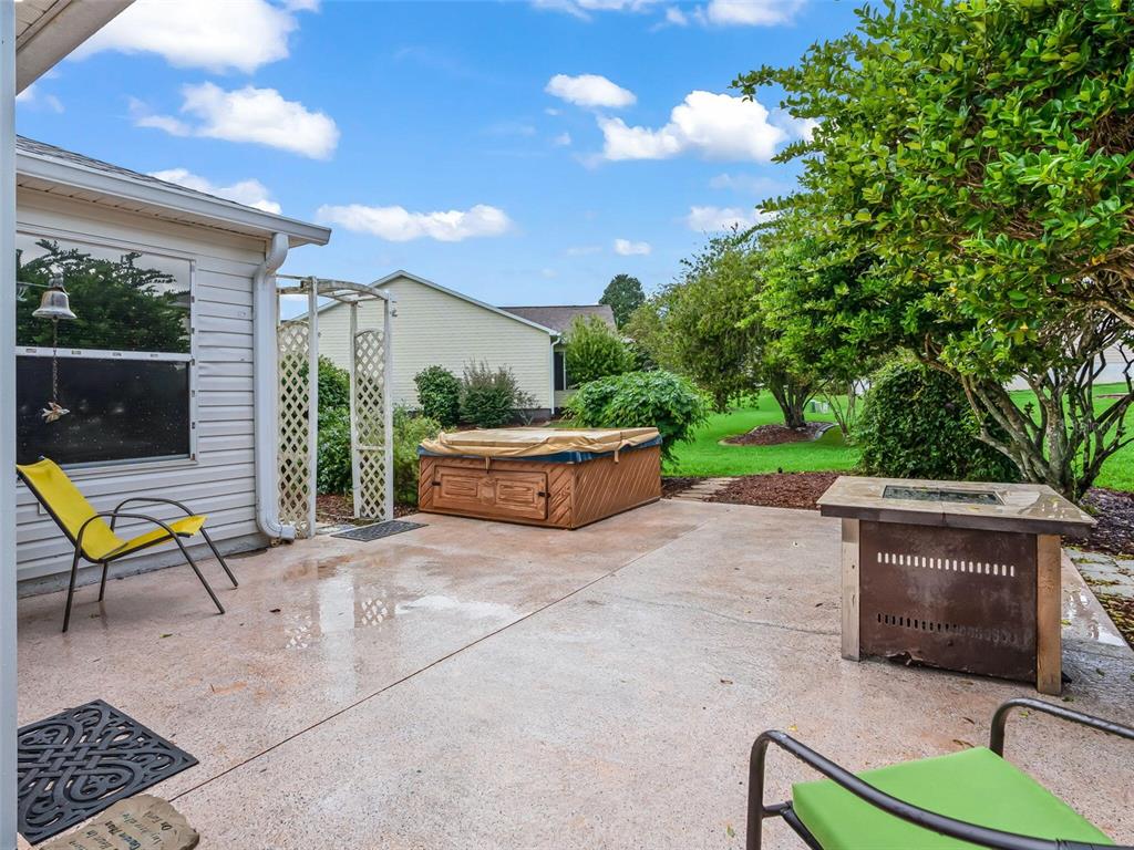 A concrete patio features a hot tub, a fire pit, and outdoor chairs near a house — 9671 SE 168TH MAPLESONG LANE, THE VILLAGES, FL