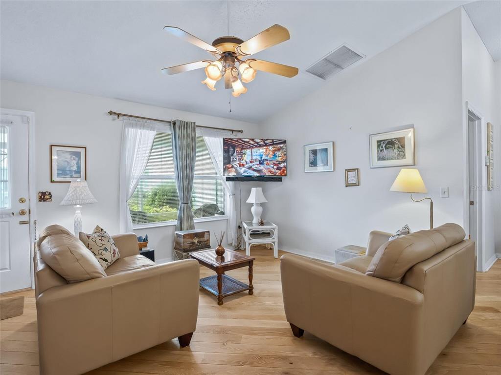 A living room features two tan leather sofas, a ceiling fan, and light wood flooring — 9671 SE 168TH MAPLESONG LANE, THE VILLAGES, FL