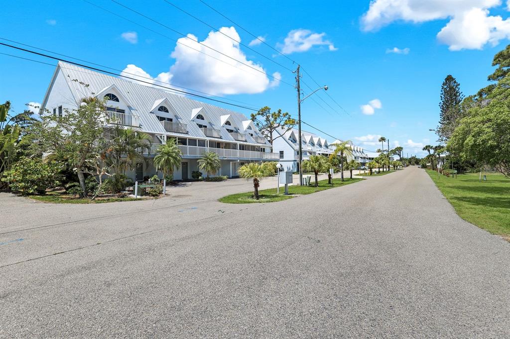 A multi-story white residential building with metal roofs sits along a paved street — 6800 PLACIDA ROAD UNIT TH13, ENGLEWOOD, FL