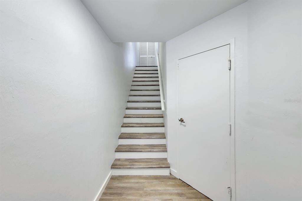 A staircase with wood-look treads leads upward between white walls next to a closed door — 6800 PLACIDA ROAD UNIT TH13, ENGLEWOOD, FL