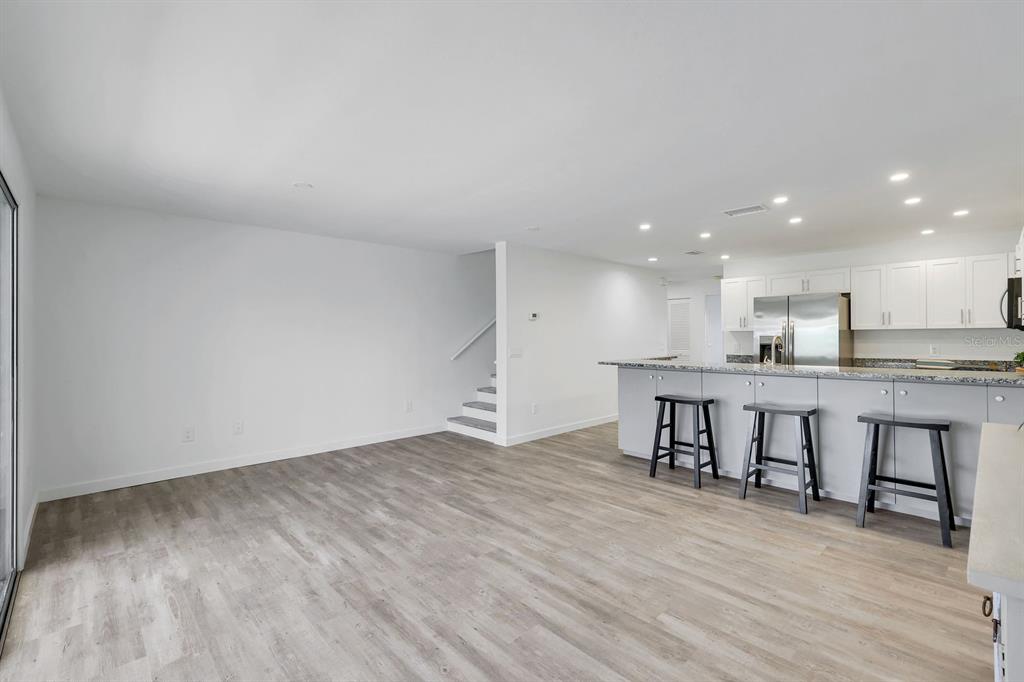 An open-concept living area features light wood-look flooring, a staircase, and a modern kitchen island — 6800 PLACIDA ROAD UNIT TH13, ENGLEWOOD, FL