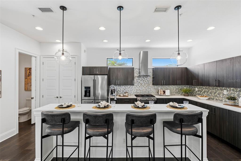 A modern kitchen features dark wood cabinets, white countertops, a breakfast bar, and pendant lighting — 300 DELMAR TERRACE S, ST PETERSBURG, FL