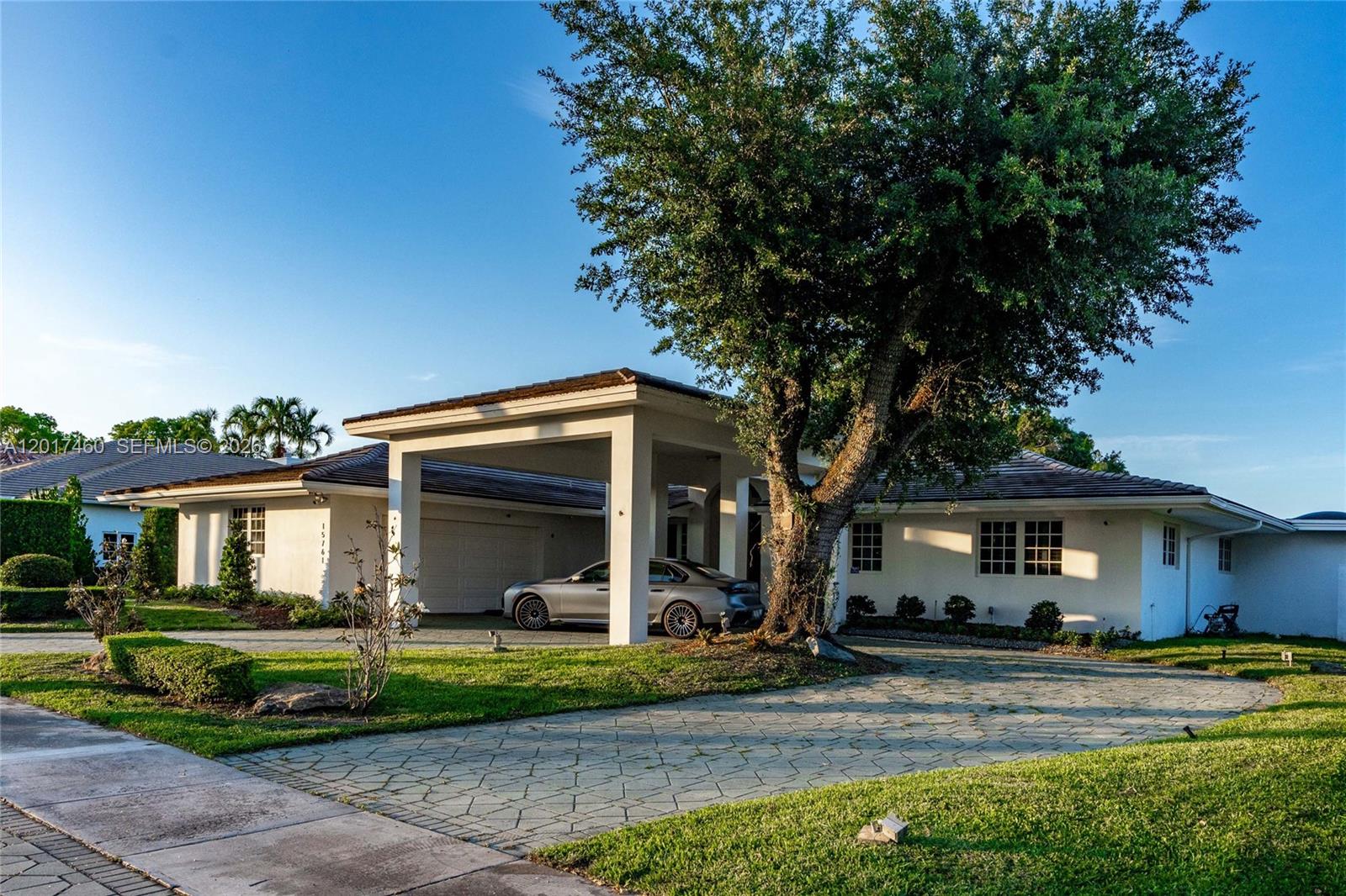 A single-story house features a large covered carport, a stone driveway, and a prominent tree — 15761 Turnberry Dr, Miami Lakes FL 33014, MIAMI LAKES, FL