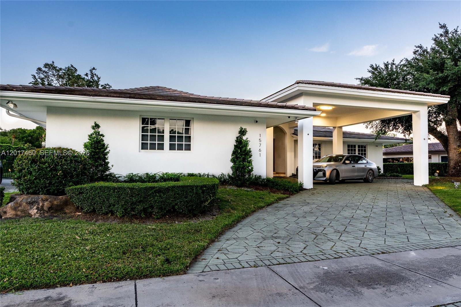 A white single-story house features a paved driveway, a covered carport, and manicured landscaping — 15761 Turnberry Dr, Miami Lakes FL 33014, MIAMI LAKES, FL