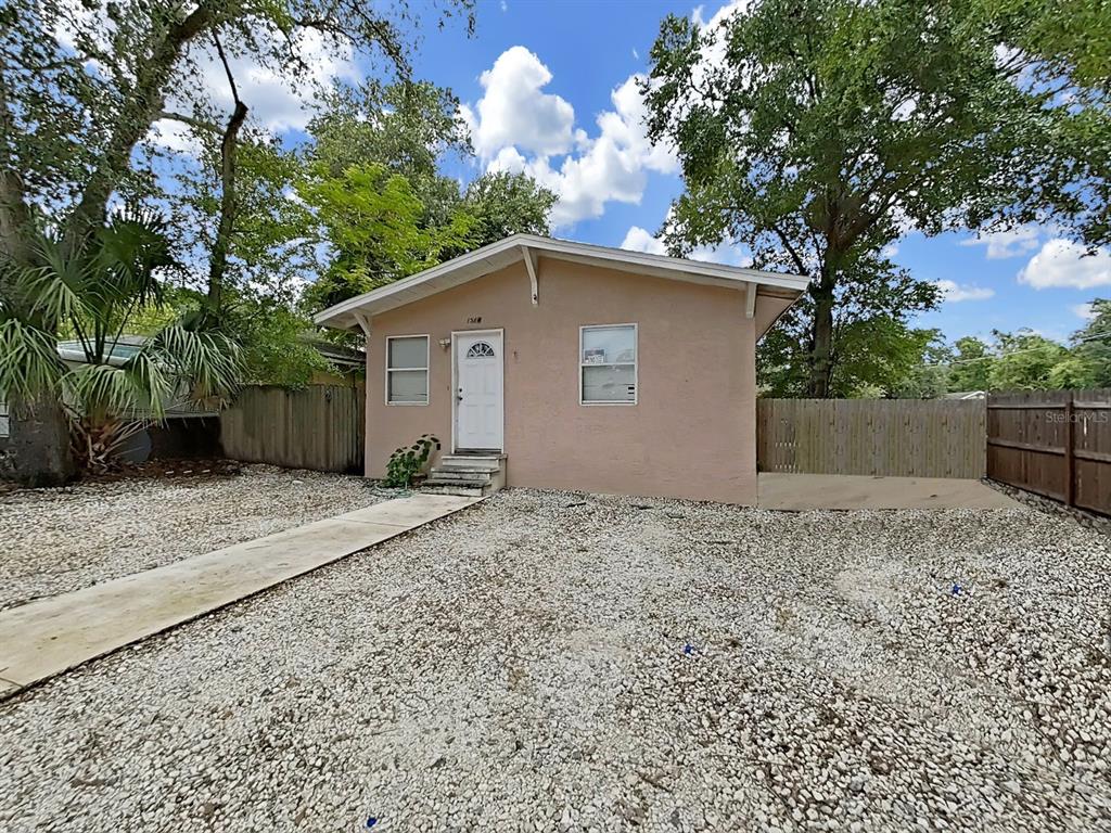 A single-story house with a tan stucco exterior, white door, and a gravel front yard — 1514 E NORTH BAY STREET, TAMPA, FL