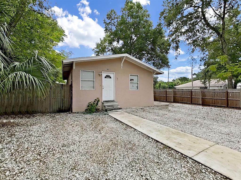 A small, tan, single-story house with a white door and gravel yard under a blue sky — 1514 E NORTH BAY STREET, TAMPA, FL