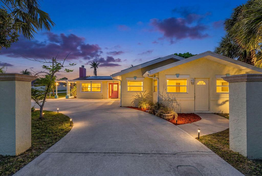 A yellow single-story house with a concrete driveway and a red front door at dusk — 614 SE Flamingo Avenue, Stuart FL 34996, STUART, FL