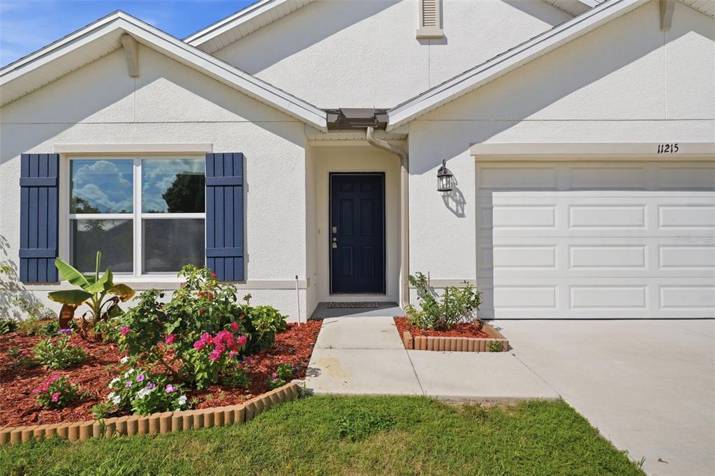 A single-story house exterior features a white stucco facade, blue shutters, and a front entrance — 11215 MURRAYSVILLE DRIVE, SPRING HILL, FL