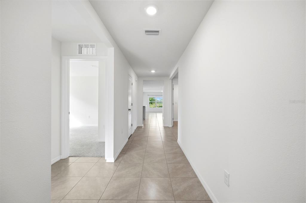 A hallway with light-colored tile flooring leads toward an open living area with a window — 11215 MURRAYSVILLE DRIVE, SPRING HILL, FL