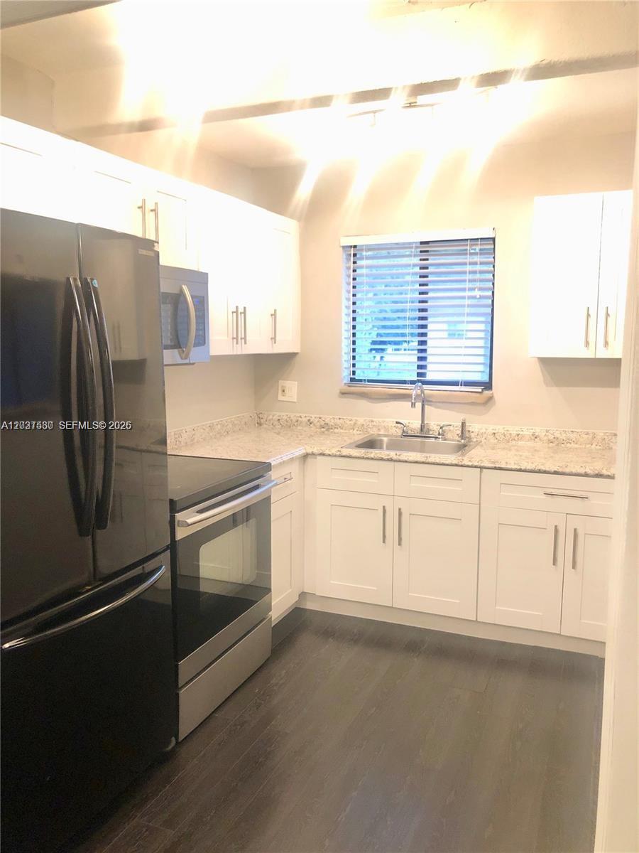 A kitchen features white cabinets, granite countertops, stainless steel appliances, and dark wood flooring — 1265 S Flagler Ave # 217, Pompano Beach FL 33060, POMPANO BEACH, FL