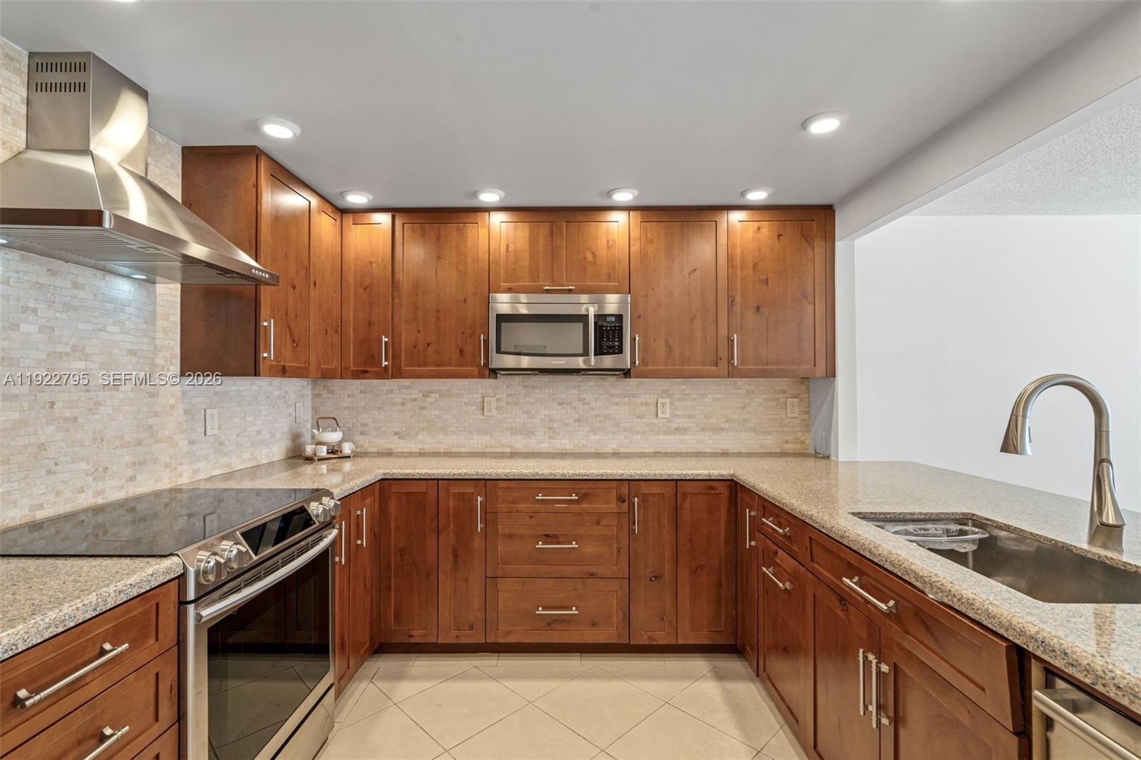 A kitchen features wood cabinets, granite countertops, stainless steel appliances, and a tiled backsplash — 1865 Brickell Ave # A1013, Miami FL 33129, MIAMI, FL