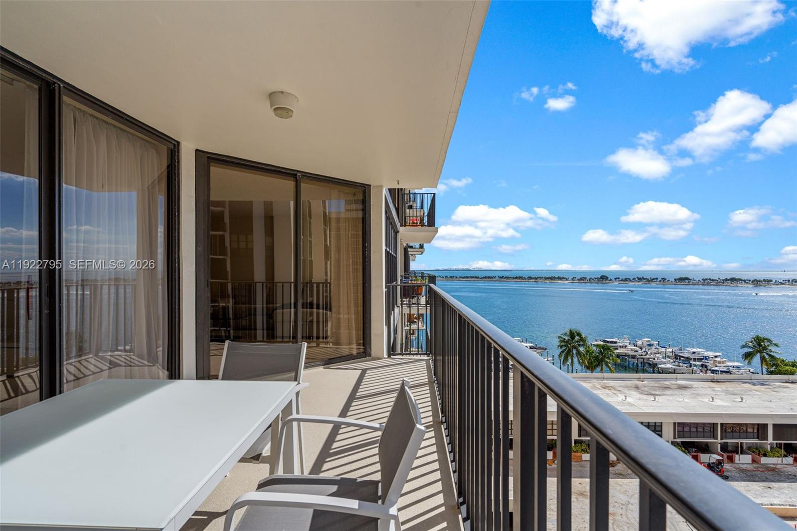 A balcony with outdoor furniture overlooks a marina and the ocean under a blue sky — 1865 Brickell Ave # A1013, Miami FL 33129, MIAMI, FL
