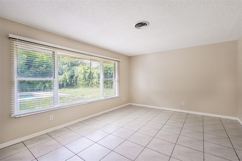 An empty room features beige walls, light-colored tile flooring, and a large window with blinds — 806 HIGHLAND DRIVE, ALTAMONTE SPRINGS, FL