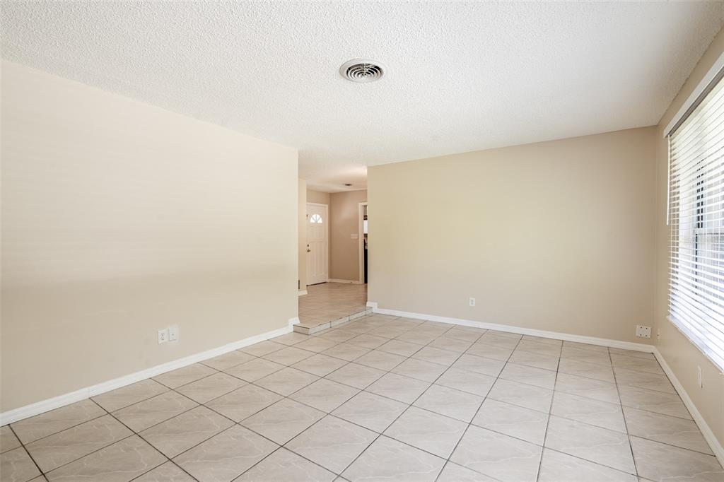 An empty room features beige walls, large square floor tiles, and a white popcorn ceiling — 806 HIGHLAND DRIVE, ALTAMONTE SPRINGS, FL