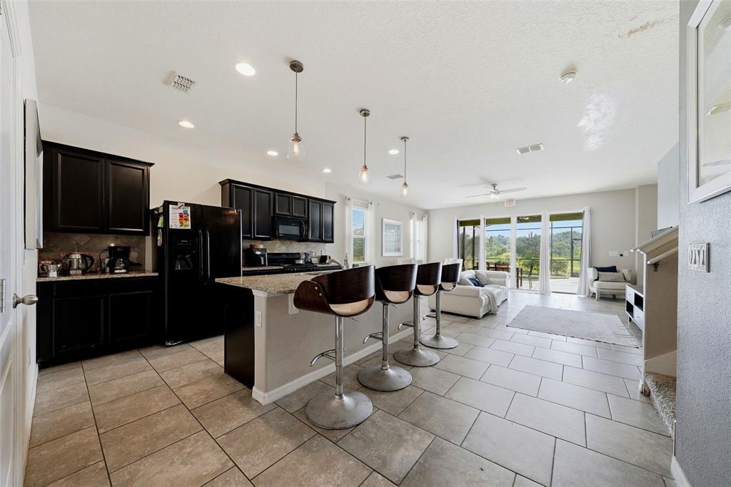 A kitchen with dark cabinets and a granite island with bar stools overlooks a living area — 4715 TERRASONESTA DRIVE, DAVENPORT, FL