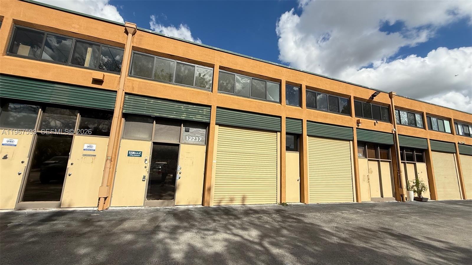 A row of commercial warehouse units features yellow stucco walls and metal roll-up doors — 12237 SW 132nd Ct # 10, Miami FL 33186, MIAMI, FL