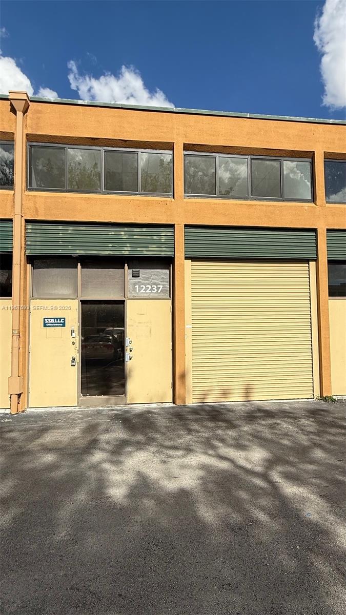 A commercial building exterior features a glass entrance door and a large metal roll-up door — 12237 SW 132nd Ct # 10, Miami FL 33186, MIAMI, FL