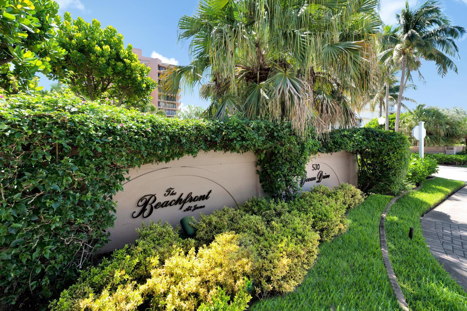 A beige sign for a beachfront property is surrounded by lush green landscaping and palm trees — 530 Ocean Drive # 202, Juno Beach FL 33408, JUNO BEACH, FL