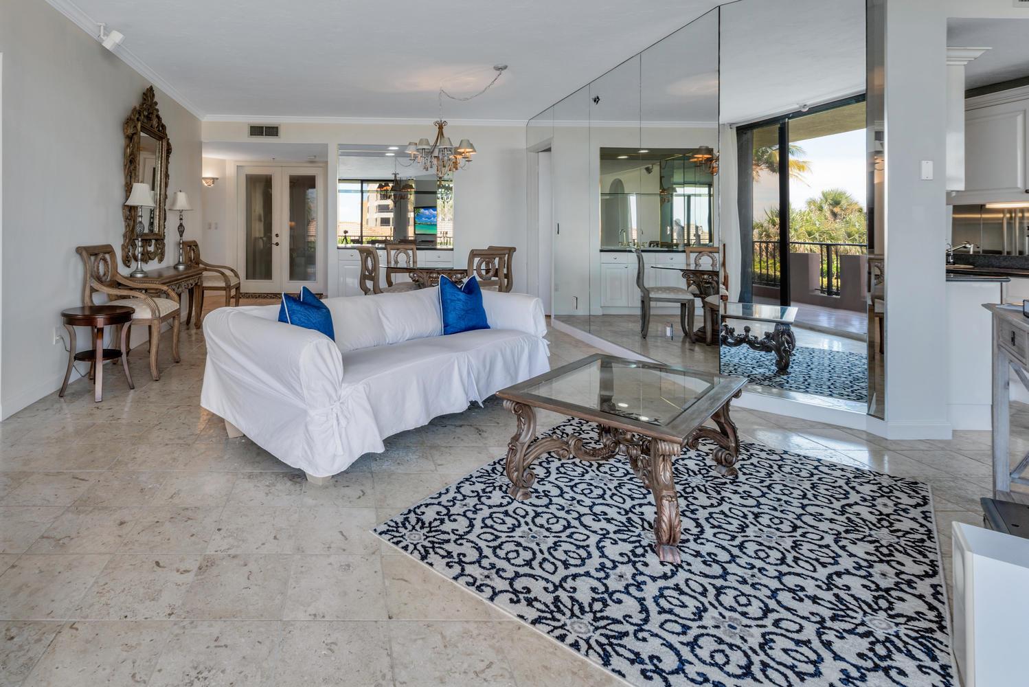 A living room with tile floors, a white sofa, a glass coffee table, and mirrored walls — 530 Ocean Drive # 202, Juno Beach FL 33408, JUNO BEACH, FL